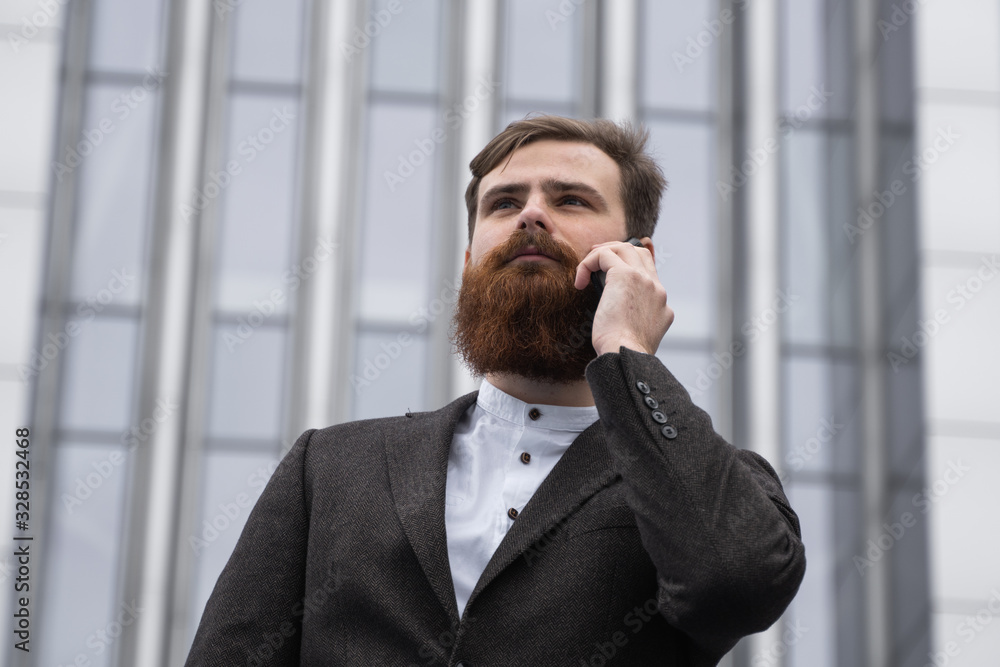 Businessman talking on the phone in financial district. Portrait of a Young urban professional man using smart phone over office building. Business man talking on his smartphone outdoors. Technology. Businessman talking on the phone in financial district. Portrait of a Young urban professional man using smart phone over office building. Business man talking on his smartphone outdoors. Technology.