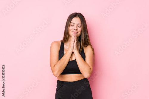 Young fitness caucasian woman isolated holding hands in pray near mouth  feels confident.