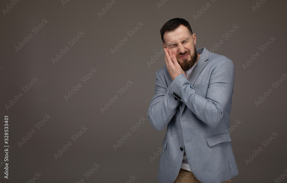 Close up portrait of nervous unhappy troubled handsome bearded man touching his cheek he has toothache isolated on gray background. Close up portrait of nervous unhappy troubled handsome bearded man touching his cheek he has toothache isolated on gray background.