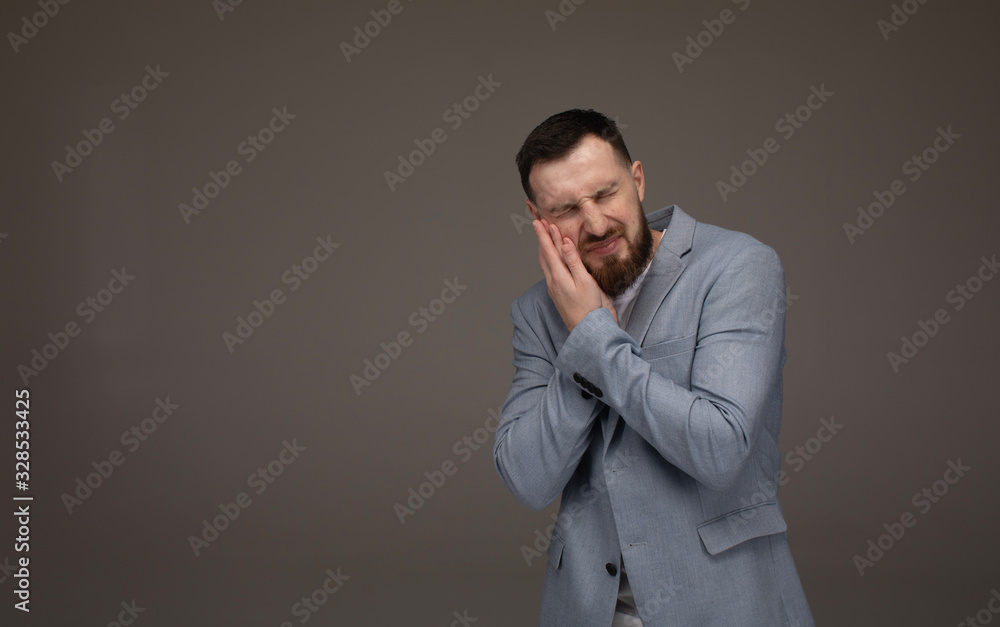 Close up portrait of nervous unhappy troubled handsome bearded man touching his cheek he has toothache isolated on gray background. Close up portrait of nervous unhappy troubled handsome bearded man touching his cheek he has toothache isolated on gray background.