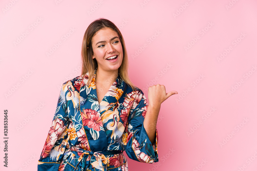 Young caucasian woman wearing pajamas points with thumb finger away, laughing and carefree. Young caucasian woman wearing pajamas points with thumb finger away, laughing and carefree.