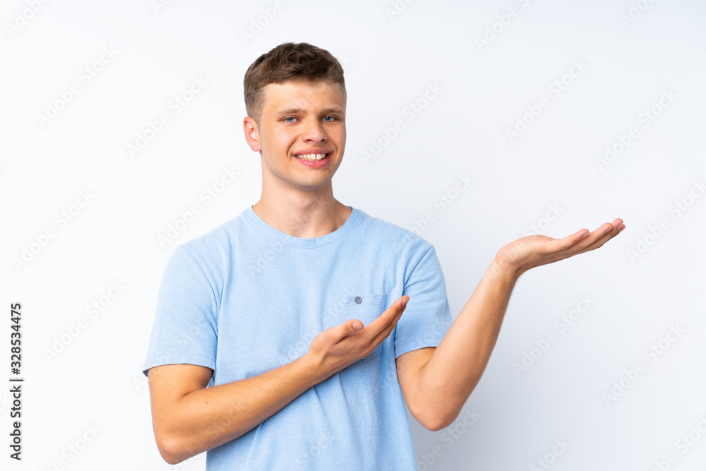 Young handsome man over isolated white background extending hands to the side for inviting to come Young handsome man over isolated white background extending hands to the side for inviting to come