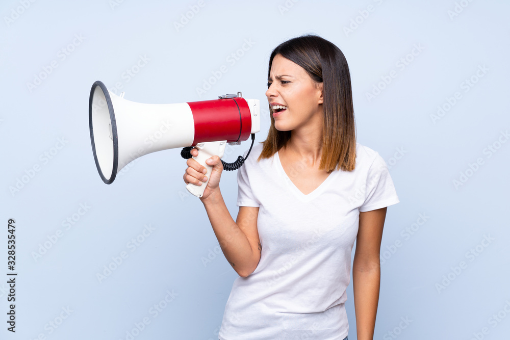 Young woman over isolated blue background shouting through a megaphone Young woman over isolated blue background shouting through a megaphone