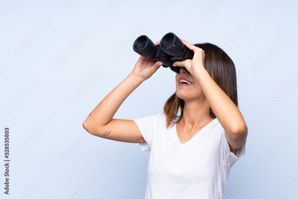 Young woman over isolated blue background with black binoculars Young woman over isolated blue background with black binoculars