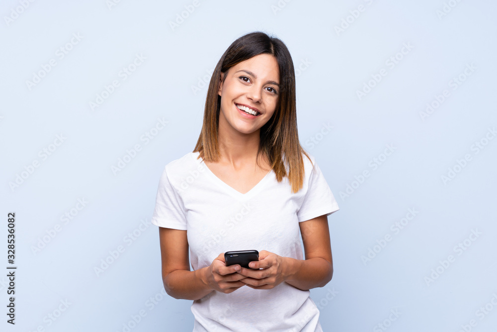 Young woman over isolated blue background sending a message or email with the mobile Young woman over isolated blue background sending a message or email with the mobile