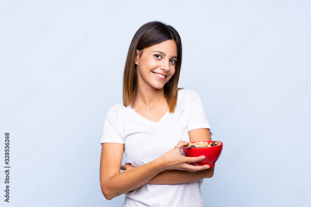 Young woman over isolated blue background holding a bowl of cereals Young woman over isolated blue background holding a bowl of cereals