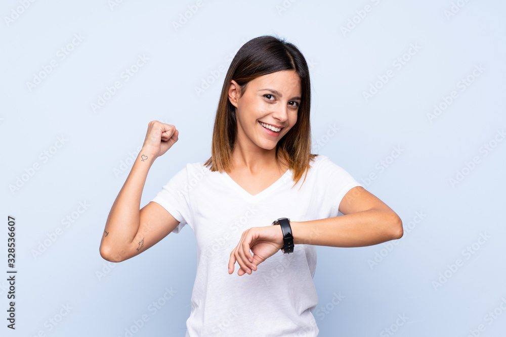 Young woman over isolated blue background with wrist watch and lucky expression Young woman over isolated blue background with wrist watch and lucky expression