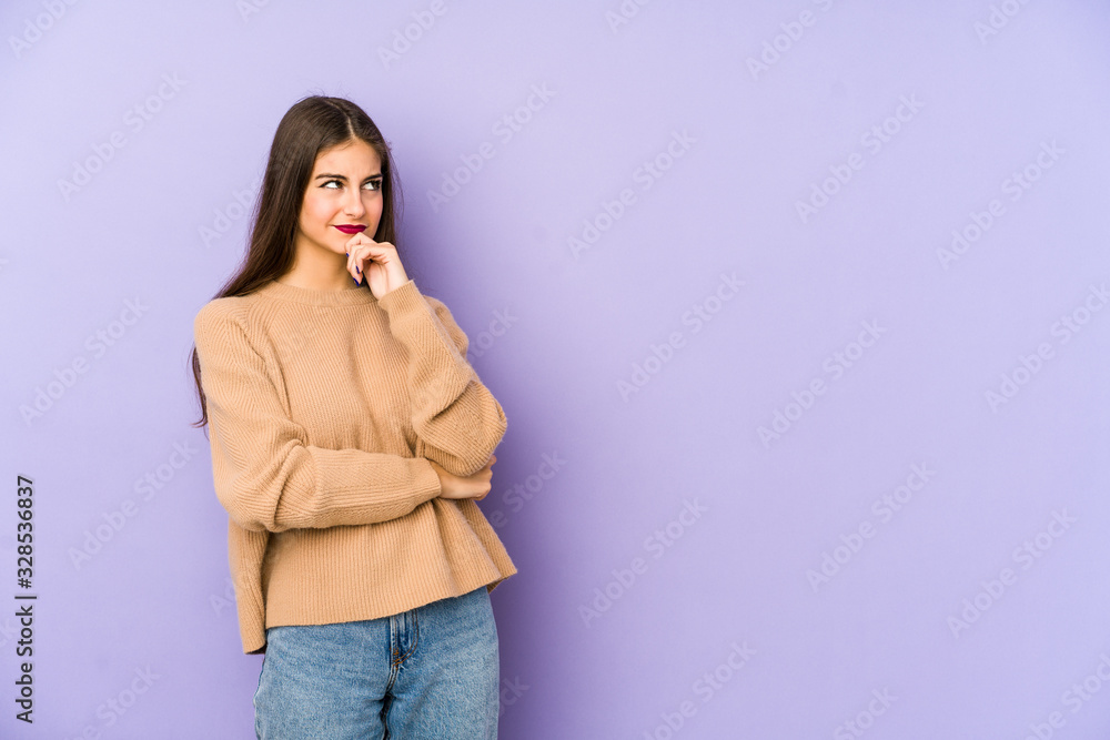 Young caucasian woman isolated on purple background relaxed thinking about something looking at a copy space. Young caucasian woman isolated on purple background relaxed thinking about something looking at a copy space.