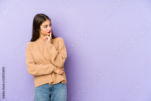 Young caucasian woman isolated on purple background looking sideways with doubtful and skeptical expression. © Asier