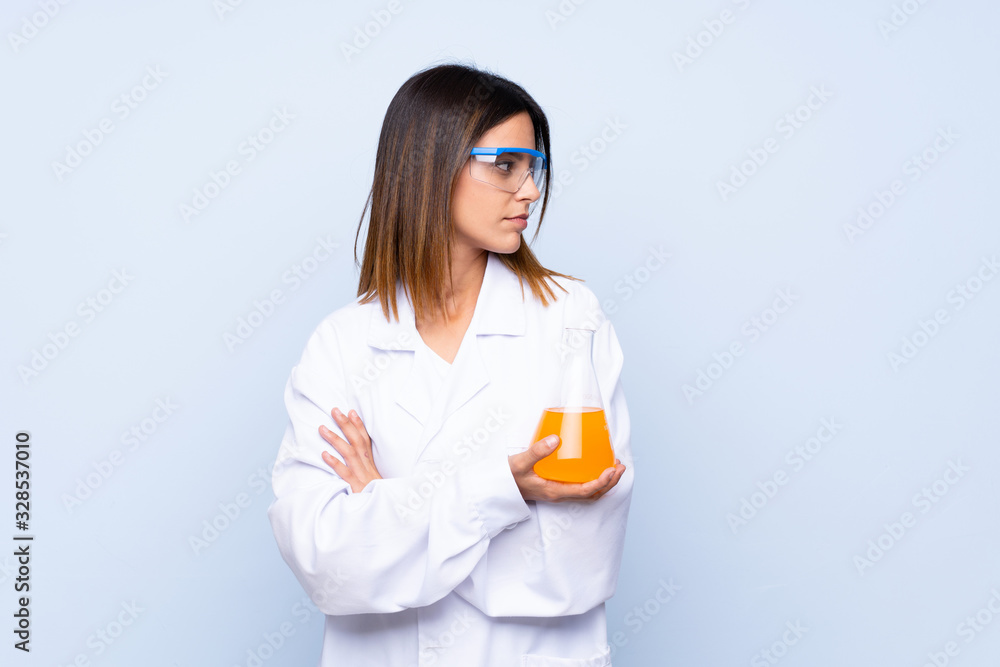 Young woman over isolated blue background with a scientific test tube and looking lateral Young woman over isolated blue background with a scientific test tube and looking lateral