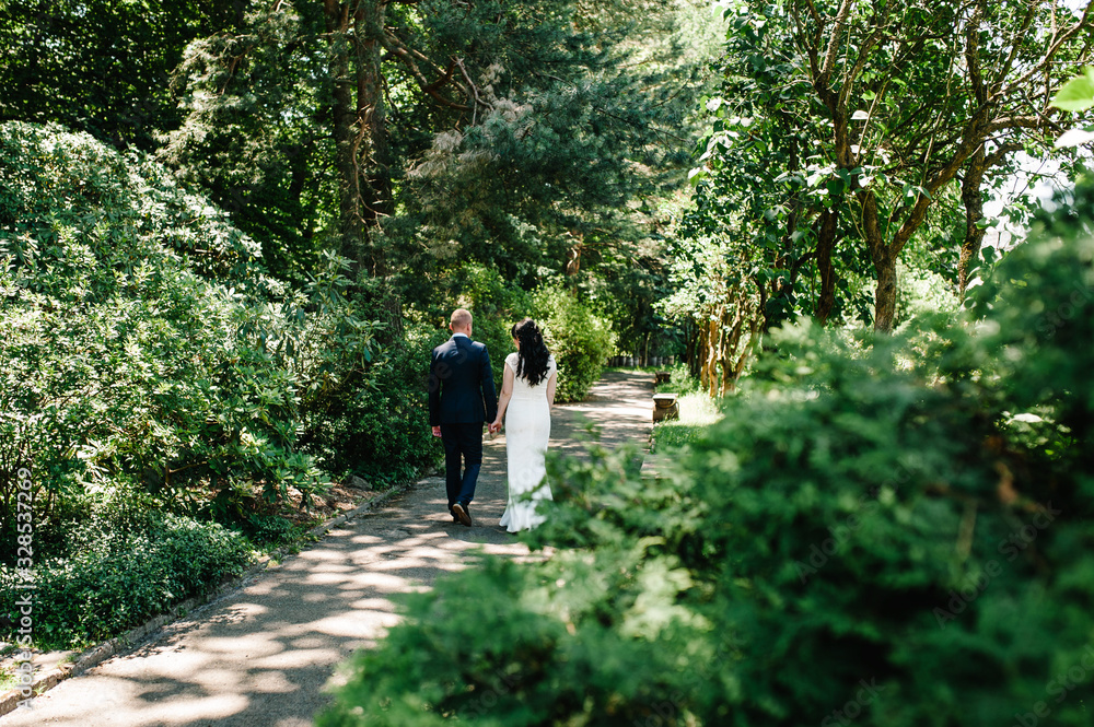 Bride, groom walking on way summer park, forest. A newlywed wedding couple running on a country straight road for their honeymoon. Rear view. Bride, groom walking on way summer park, forest. A newlywed wedding couple running on a country straight road for their honeymoon. Rear view.