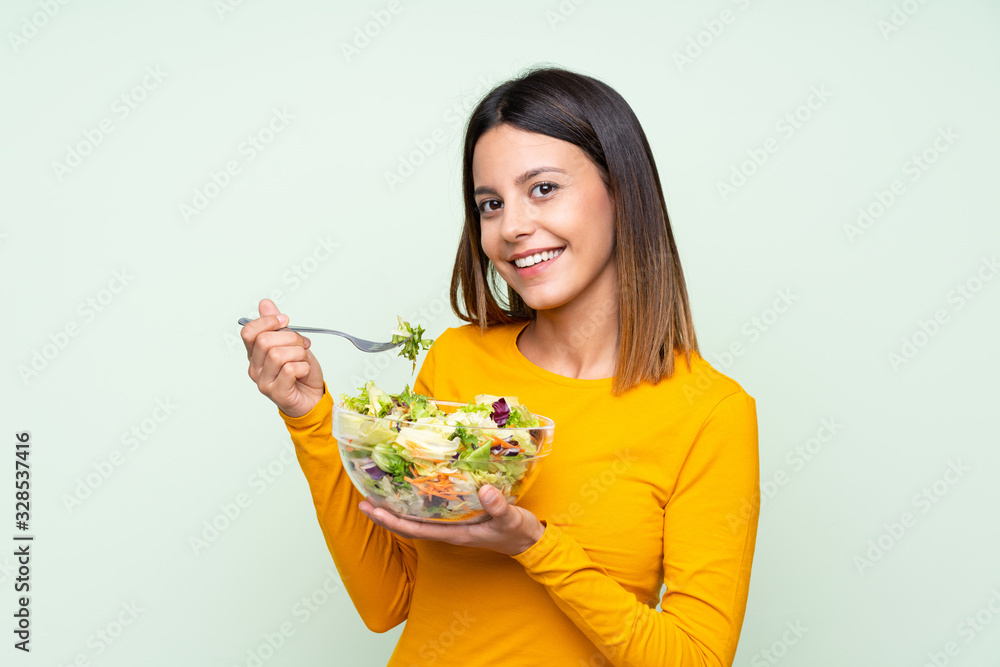 Young woman with salad over isolated green wall Young woman with salad over isolated green wall