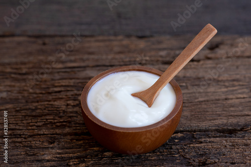 Natural homemade plain organic yogurt in wooden bowl and wood spoon on wood texture background