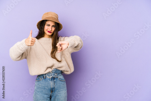 Young caucasian woman isolated on purple background showing thumbs up and thumbs down, difficult choose concept