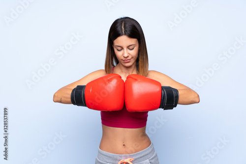 Young sport woman over isolated blue background with boxing gloves