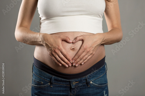 Big belly of a pregnant woman on a gray background. Close-up. © Анна Демидова