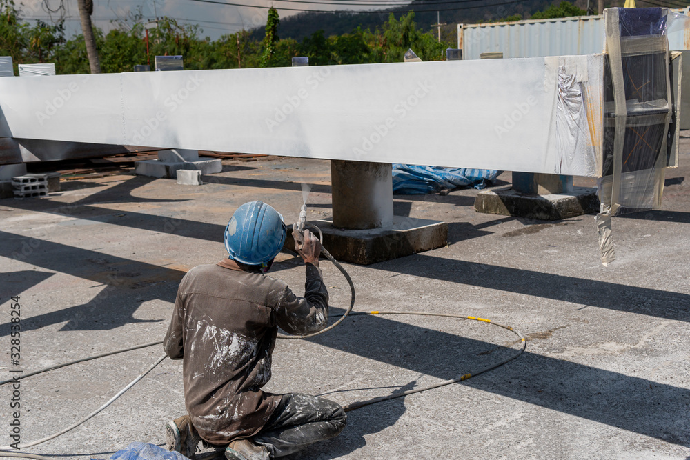 The painter is working to fireproof paint on steel structure with spray gun, at industrial factory.