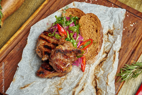 Appetizing pork kebab with spices and onions on a wooden tray on wooden background. Shahlik. Portion of grilled meat. Top view, flat lay photo