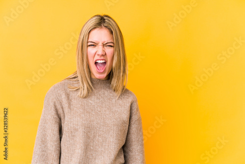 Young blonde caucasian woman isolated on yellow background shouting very angry, rage concept, frustrated.