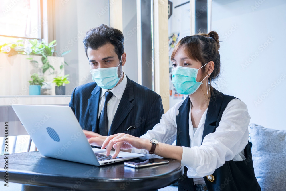 sian female and Businessman workers meeting together with laptop and wear protective masks prevent PM 2.5 and corona viruus or covic19 at co working space .Health and teamwork concept sian female and Businessman workers meeting together with laptop and wear protective masks prevent PM 2.5 and corona viruus or covic19 at co working space .Health and teamwork concept