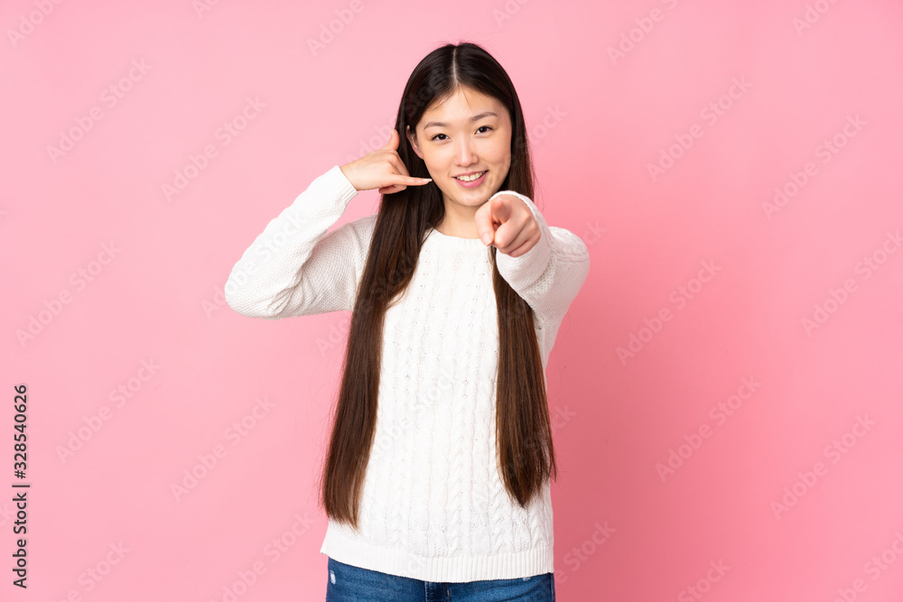 Young asian woman over isolated background making phone gesture and pointing front Young asian woman over isolated background making phone gesture and pointing front