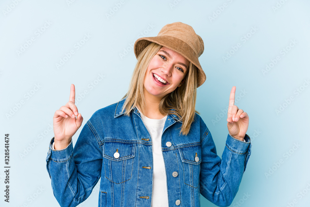Young blonde caucasian woman isolated indicates with both fore fingers up showing a blank space. Young blonde caucasian woman isolated indicates with both fore fingers up showing a blank space.