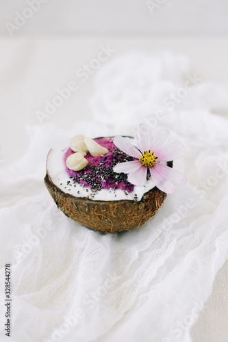healthy Breakfast berry smoothie with Chia seeds and cashew nuts in a natural coconut plate on a white table with pink flowers