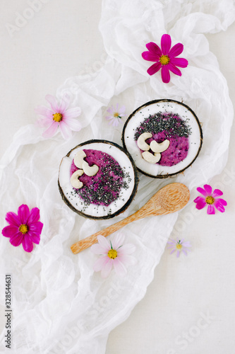 healthy Breakfast berry smoothie with Chia seeds and cashew nuts in a natural coconut plate on a white table with pink flowers