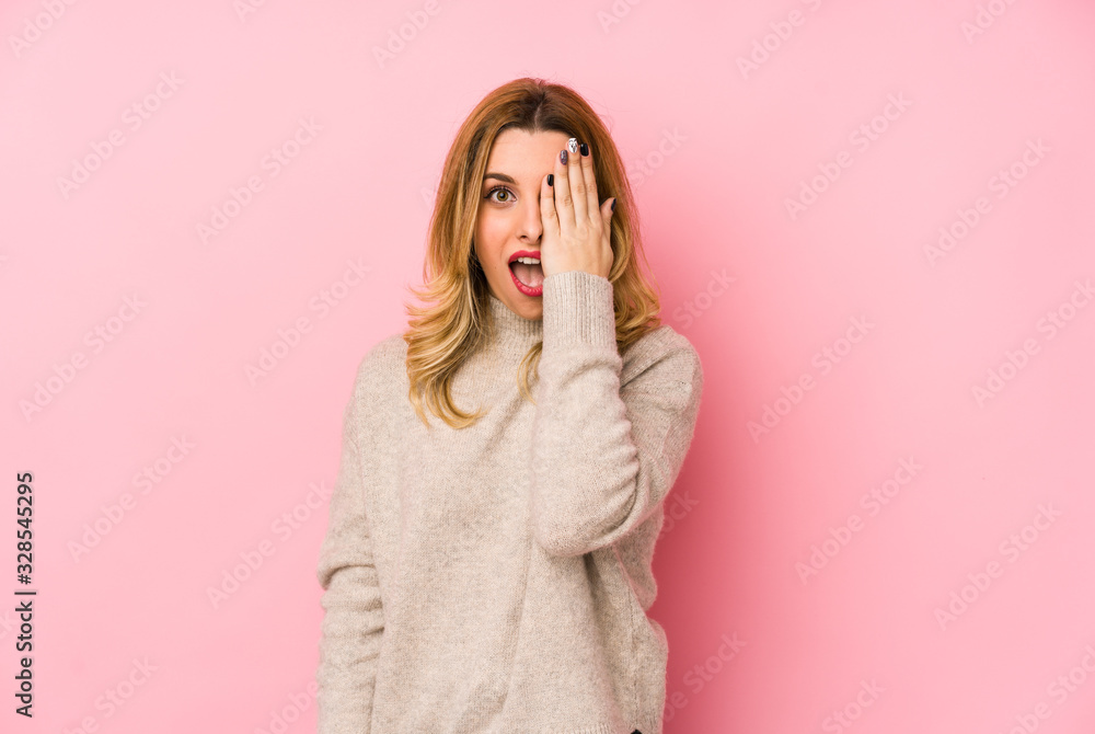 Young blonde cute woman wearing a sweater isolated having fun covering half of face with palm. Young blonde cute woman wearing a sweater isolated having fun covering half of face with palm.