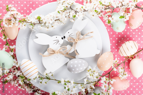 Easter table setting, holiday table home decor idea, flat lay composition with white plates, cutlery, colorful pastel painted Easter eggs, festive decor and fresh spring flowers photo