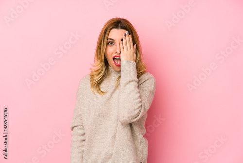 Young blonde cute woman wearing a sweater isolated having fun covering half of face with palm.