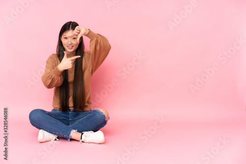 Young asian woman sitting on the floor isolated on pink background focusing face. Framing symbol