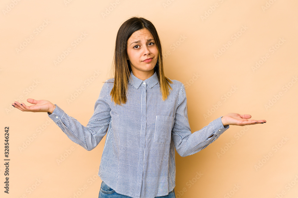 Young woman isolated on beige background doubting and shrugging shoulders in questioning gesture. Young woman isolated on beige background doubting and shrugging shoulders in questioning gesture.