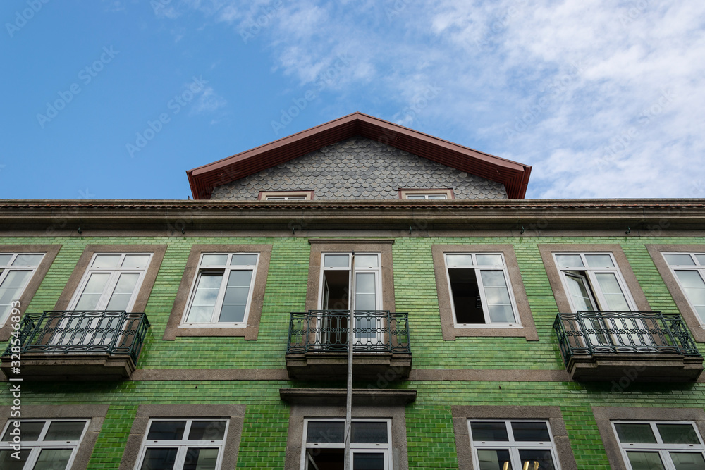 Green house, with traditional Portuguese green tiles. Blue sky and clouds