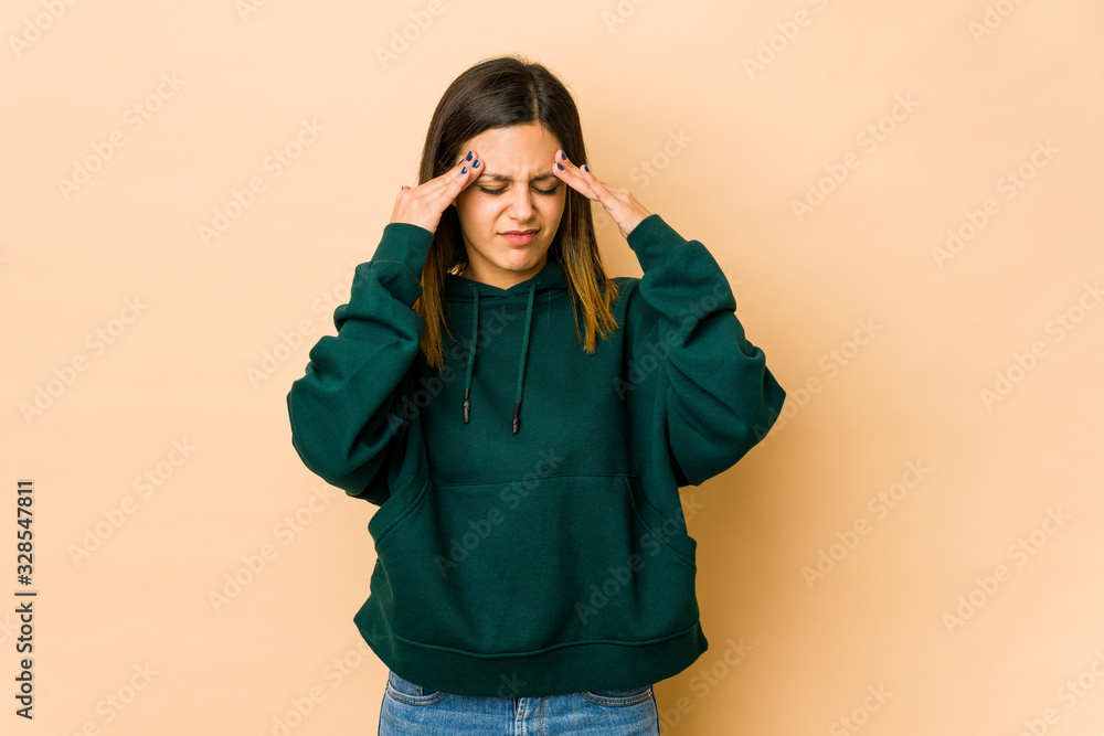 Young woman isolated on beige background having a head ache, touching front of the face. Young woman isolated on beige background having a head ache, touching front of the face.