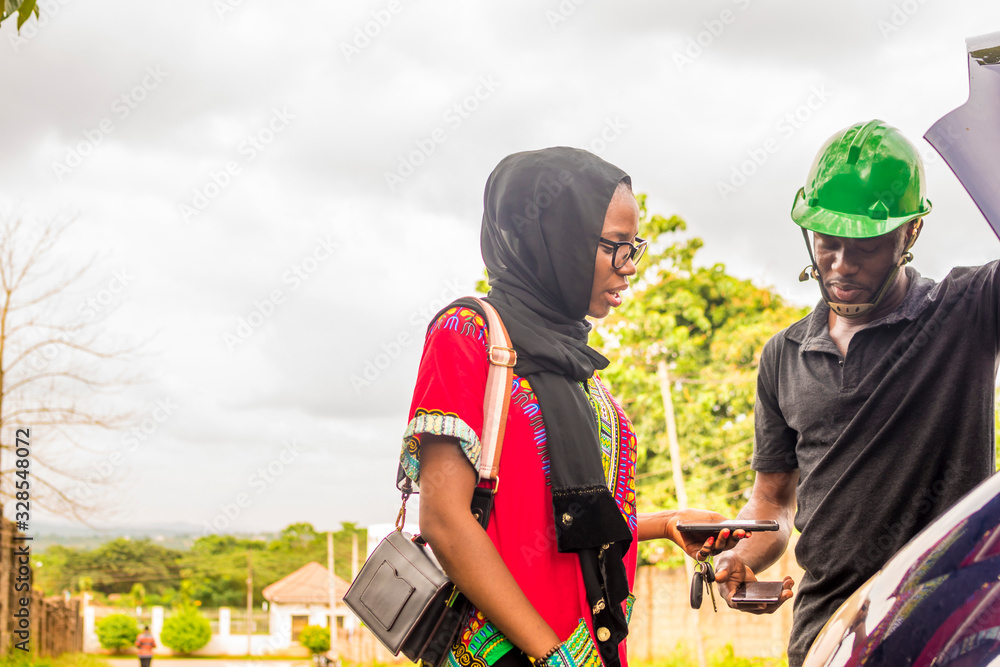 Obraz premium young african woman paying a mechanic who helped fixed her car via mobile transfer