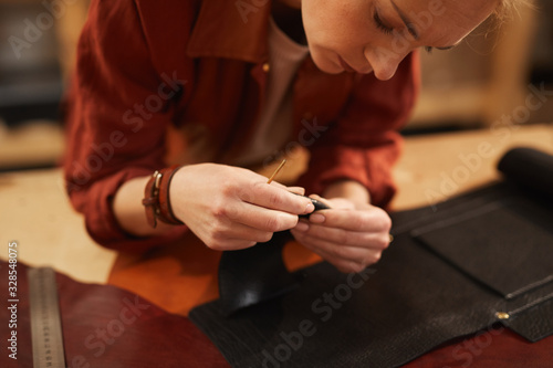 Horizontal shot of young female artisan creating something using leather materials of different colours