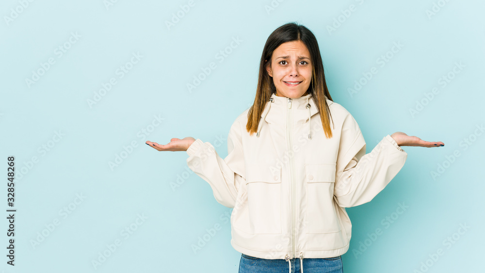 Young woman isolated on blue background confused and doubtful shrugging shoulders to hold a copy space. Young woman isolated on blue background confused and doubtful shrugging shoulders to hold a copy space.