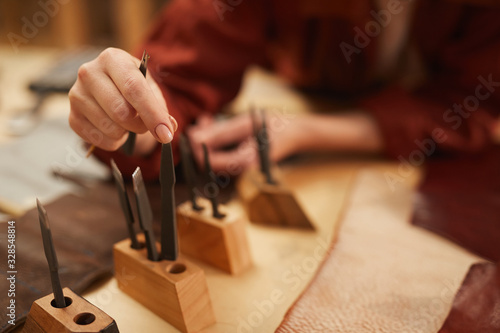 Unrecognizable craftswoman choosing tools for further work with leather, horizontal close up shot