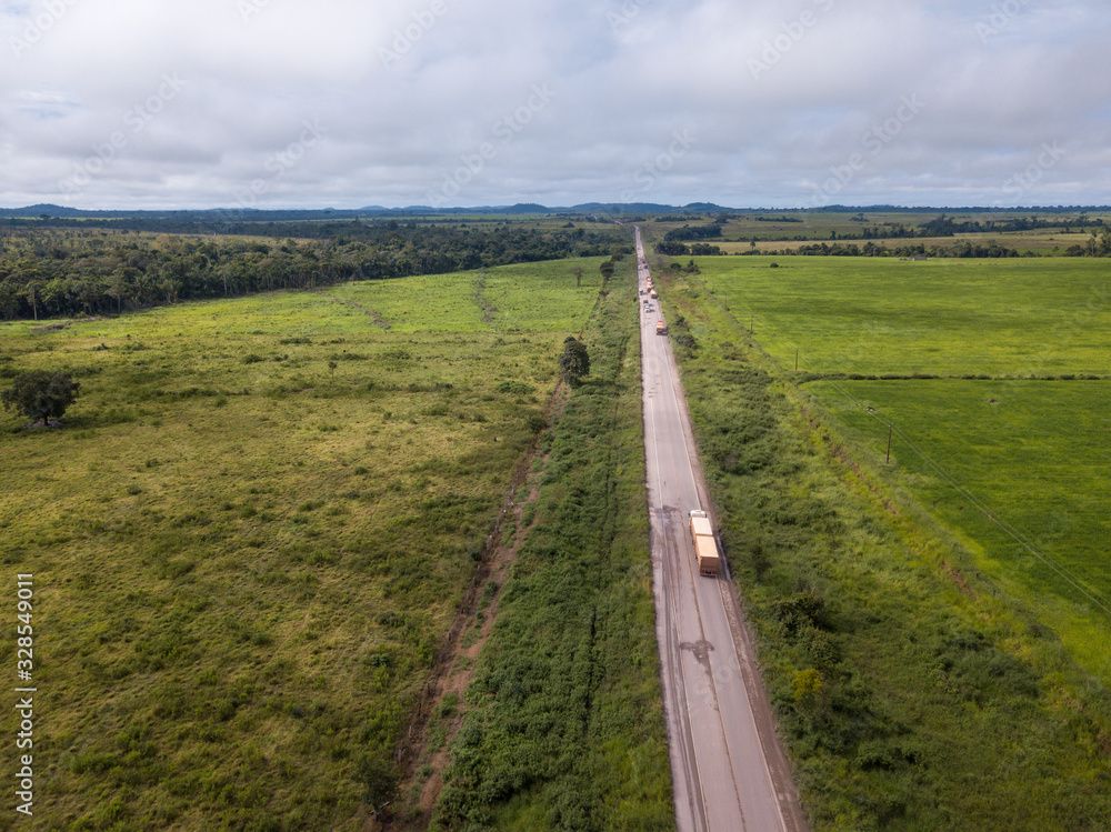 Drone aerial view of trucks transporting soy along the BR 163 road and cattle pasture farm near Novo Progresso city in the Amazon. Rainforest area and deforestation in the background. Para, Brazil.