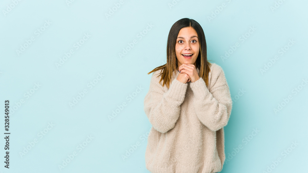 Young woman isolated on blue background praying for luck, amazed and opening mouth looking to front. Young woman isolated on blue background praying for luck, amazed and opening mouth looking to front.