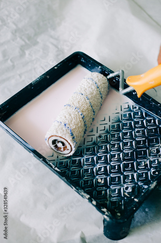 the roller is wetted in a liquid primer in a plastic black container, before painting the walls with paint photo