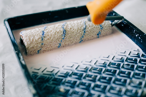 the roller is wetted in a liquid primer in a plastic black container, before painting the walls with paint photo