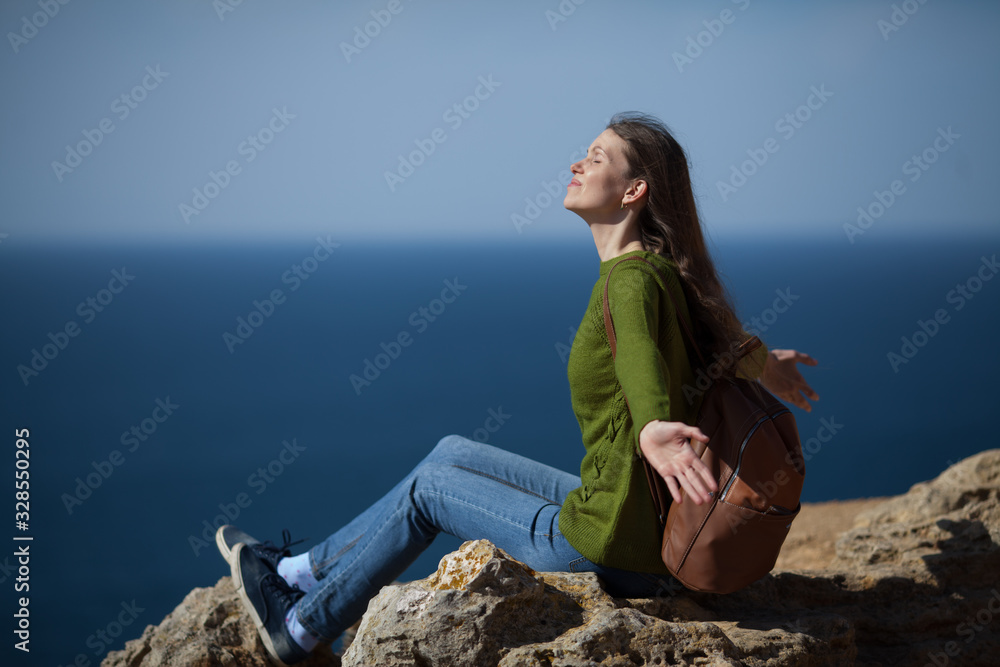 A beautiful young woman traveler with a backpack on the background of the sea opened her arms. Copy space. The concept of freedom , travel and an active lifestyle.