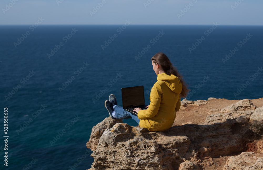 A freelancer girl is working typing on a laptop and looking at a monitor with a beautiful view of the open air sea sky. Traveling with a computer. Online dream job.