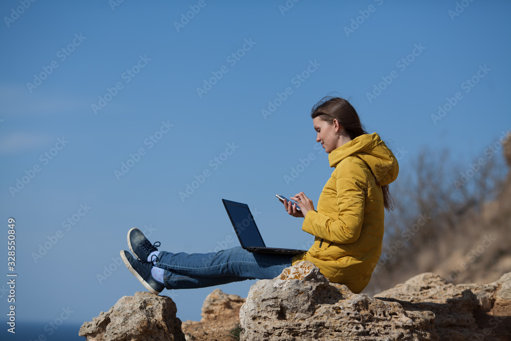 A freelancer girl working on a laptop and mobile phone with a beautiful view of the open air sea sky. Traveling with a computer. Online dream job.