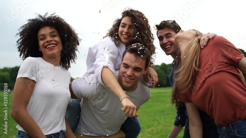 Group of four friends having fun at the park blowing confetti - Millennials playing together at sunset photo