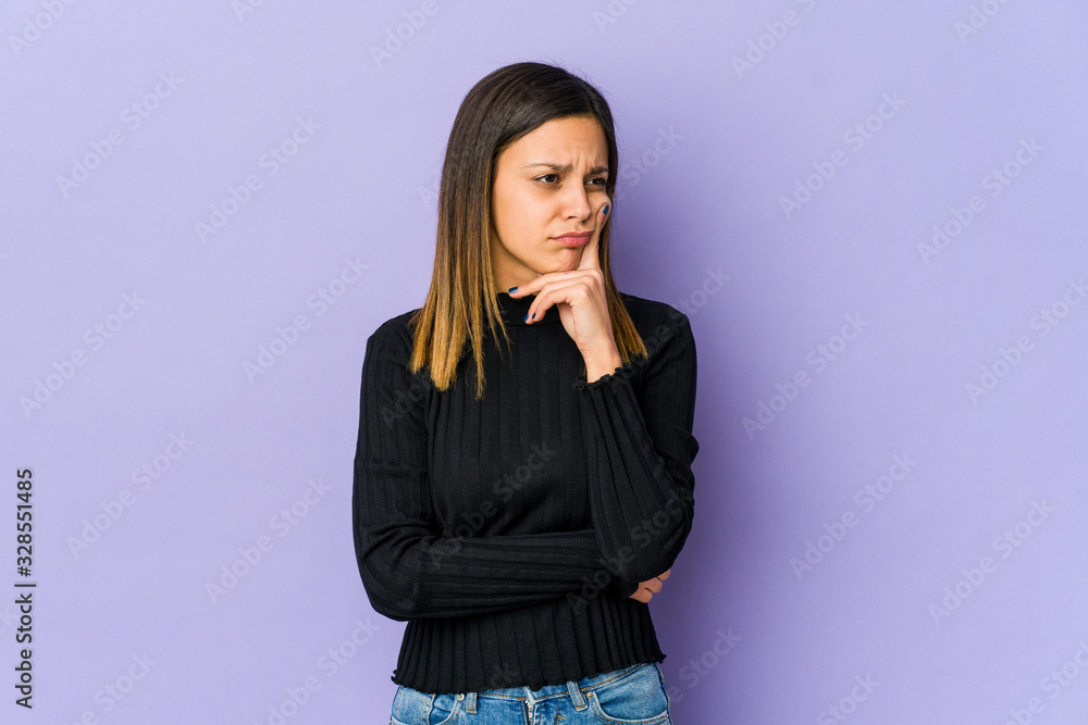 Young woman isolated on purple background contemplating, planning a strategy, thinking about the way of a business. Young woman isolated on purple background contemplating, planning a strategy, thinking about the way of a business.