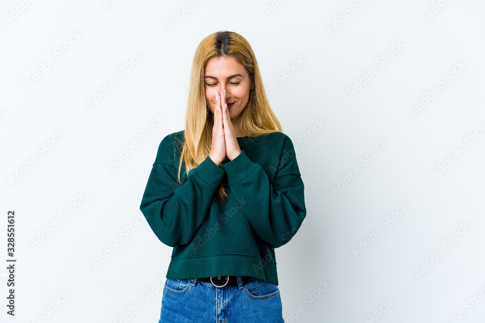Young blonde woman isolated on white background holding hands in pray near mouth, feels confident. Young blonde woman isolated on white background holding hands in pray near mouth, feels confident.