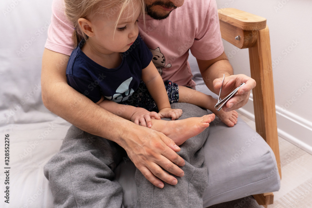 Father cuts toenail to his baby with clipper, the kid sits at fathers knees. Manicure. Father cuts toenail to his baby with clipper, the kid sits at fathers knees. Manicure.